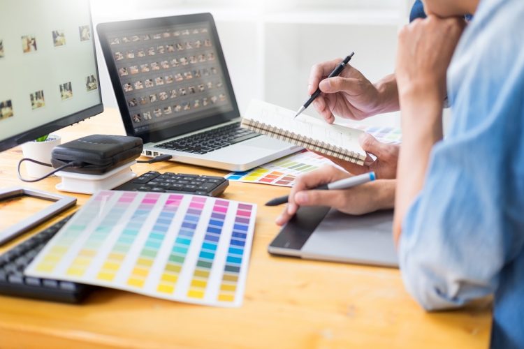 graphic designer team working on web design using color swatches editing artwork using tablet and a stylus At Desks In Busy Creative Office