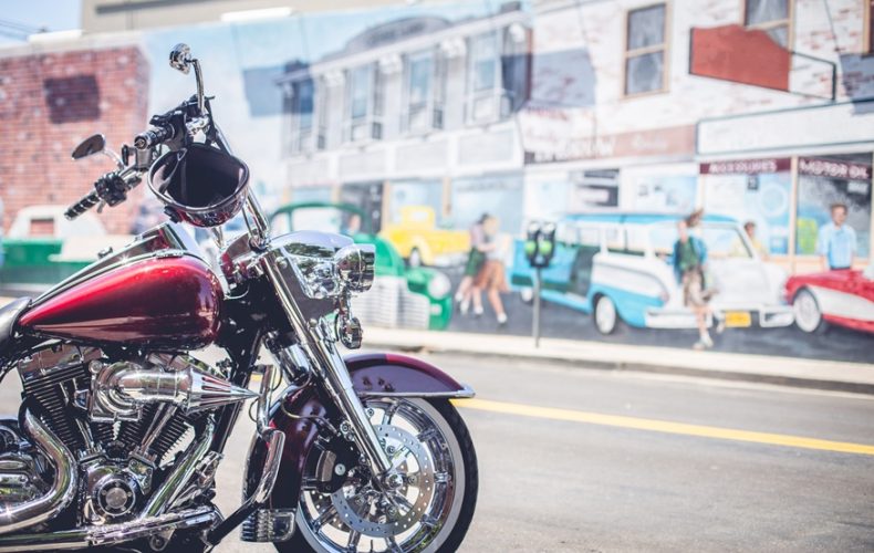 Side view of red vintage custom motorcycle parked on street near wall with graffiti in sunny day in San Francisco, USA